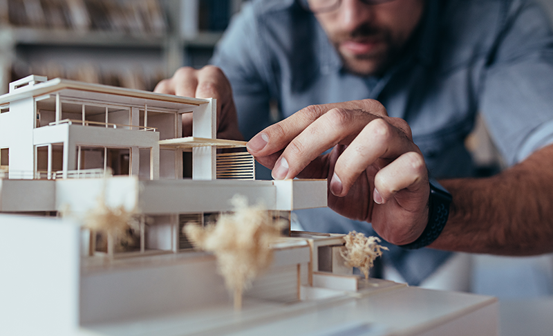 An architect Working on a Building Prototype Made of White Wood An architect Working on a Building Prototype Made of White Wood