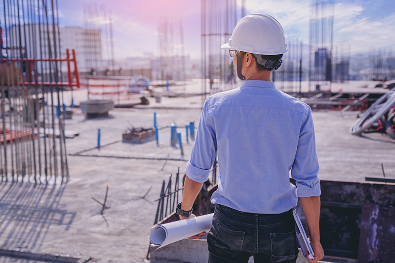 An architect at a building site observing work in progress with a set of architectural blueprints An architect at a building site observing work in progress with a set of architectural blueprints